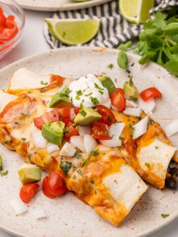 two enchiladas on a plate with sauce and sour cream.