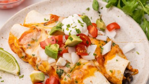 two enchiladas on a plate with sauce and sour cream.