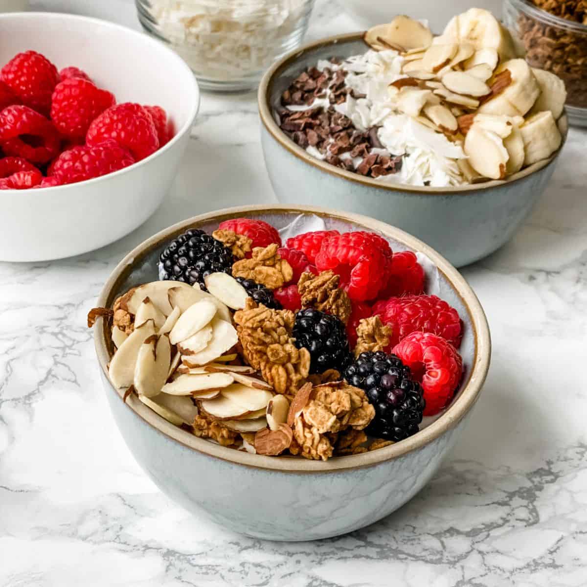 close up picture of two yogurt bowls with fruit and granola on top.