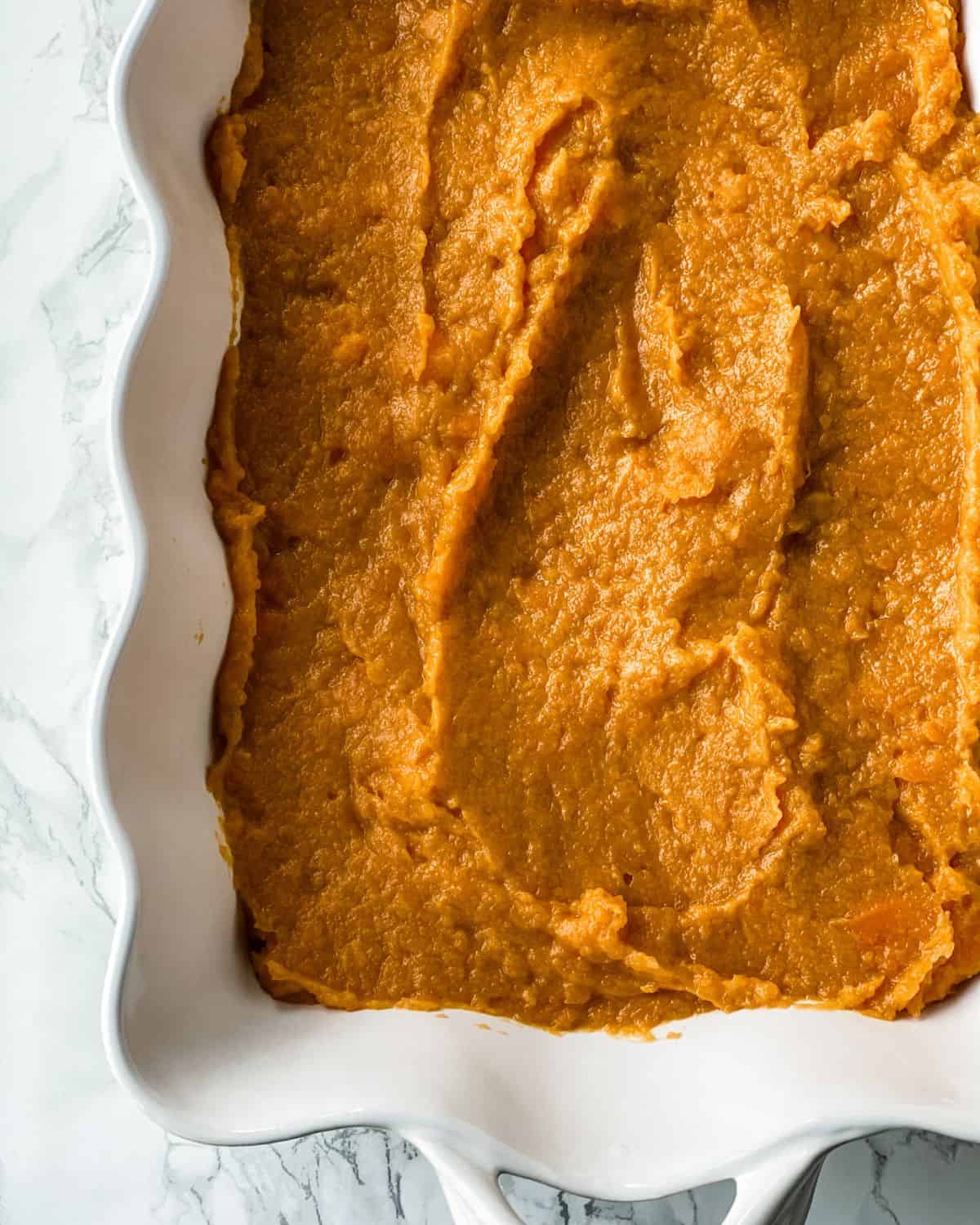 sweet potatoes filling spread into a casserole dish.