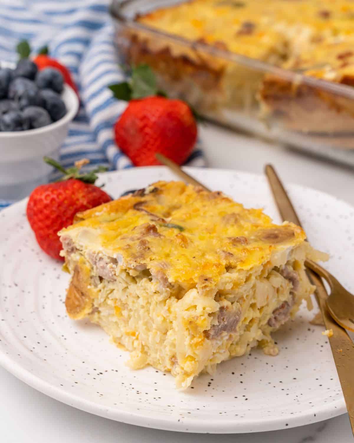 close-up front picture of a piece of overnight egg hash brown casserole with the rest of the casserole behind it in a dish.