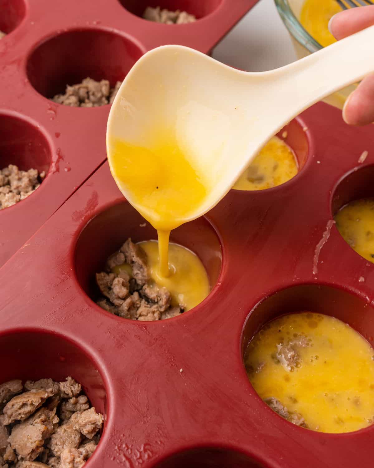 pouring egg mixture into the muffin pan cups over the sausage.