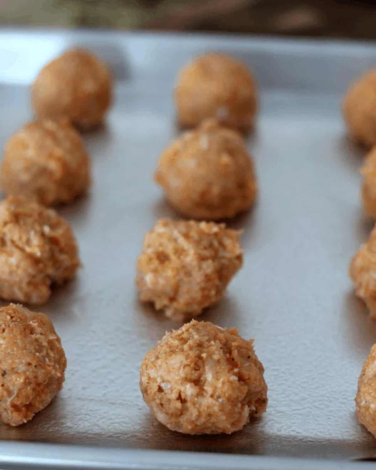 raw chicken meatballs on a baking sheet.