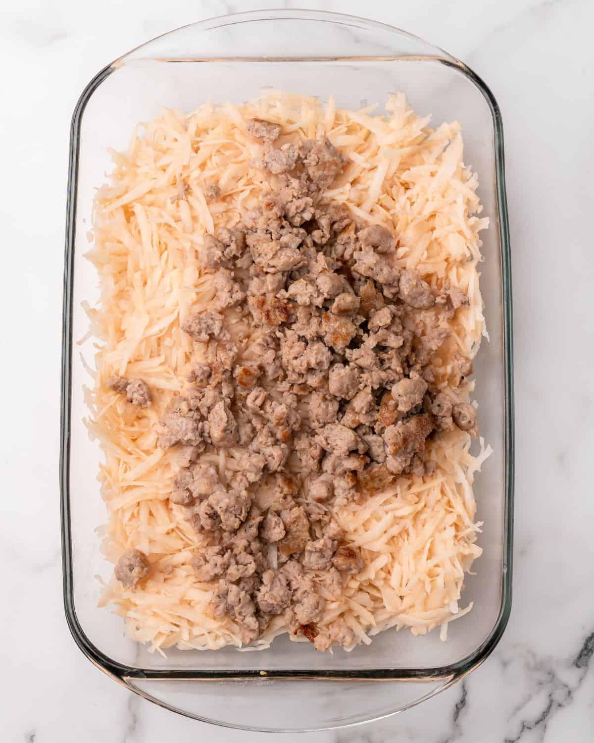 a picture showing the cooked breakfast sausage on top of the shredded hash browns in the casserole dish.