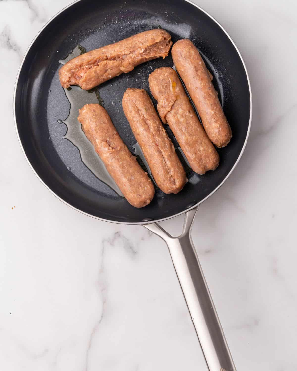 chicken sausage links in a pan with oil.