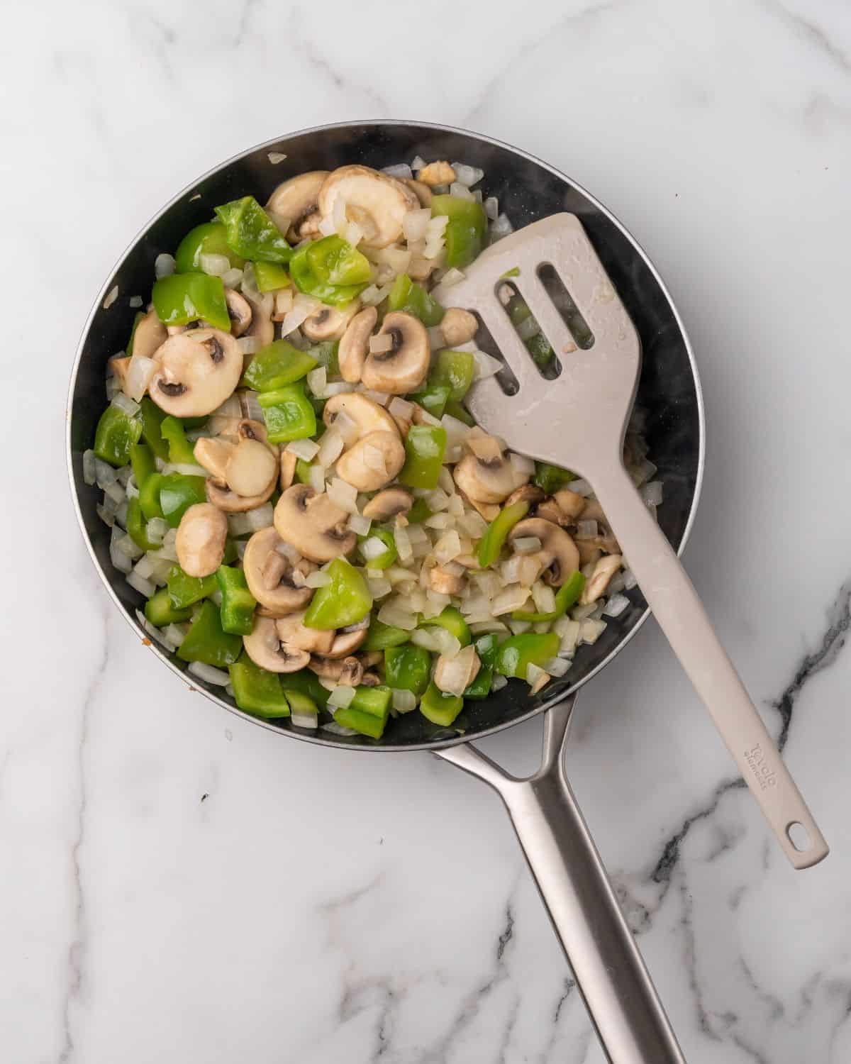 overhead picture of cooked mushrooms, onions, and peppers in a skillet.