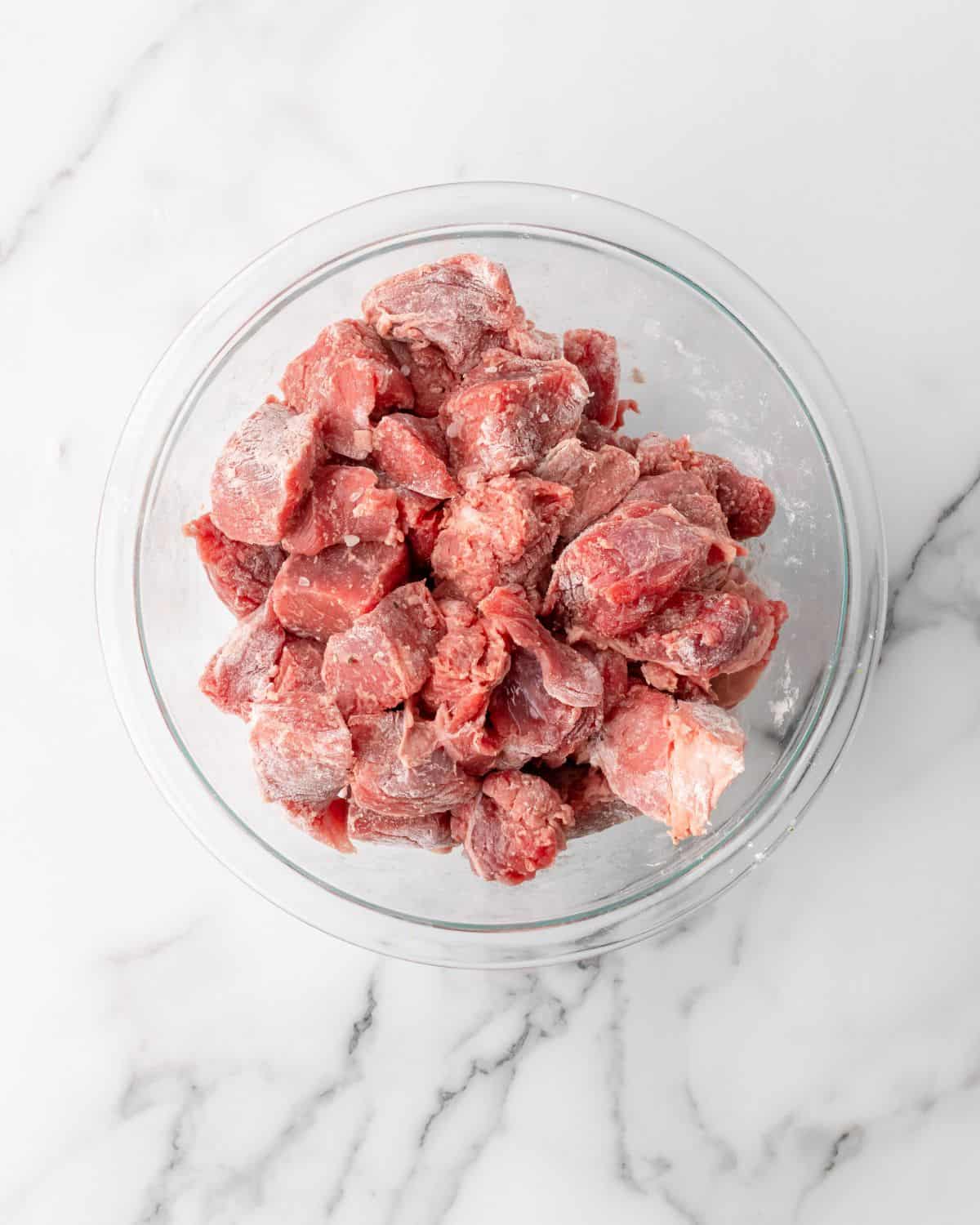 beef tossed with flour in a glass bowl.