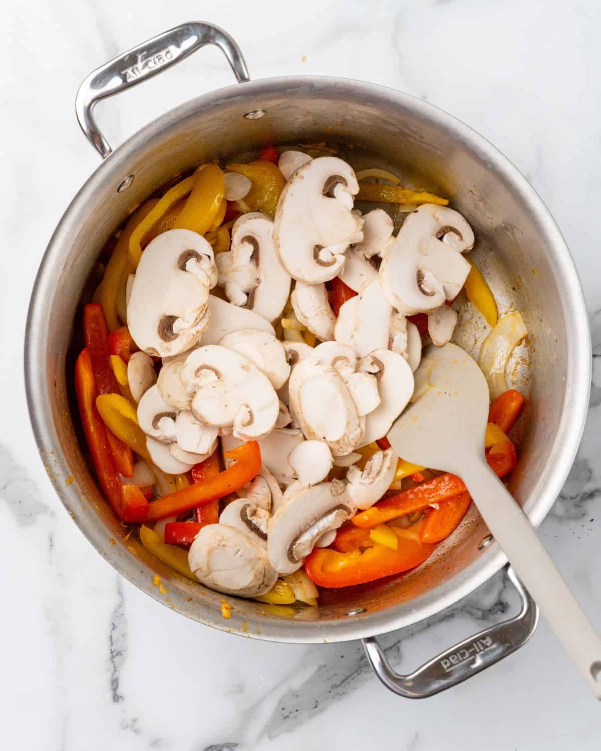 mushrooms in the pan with peppers and onions.