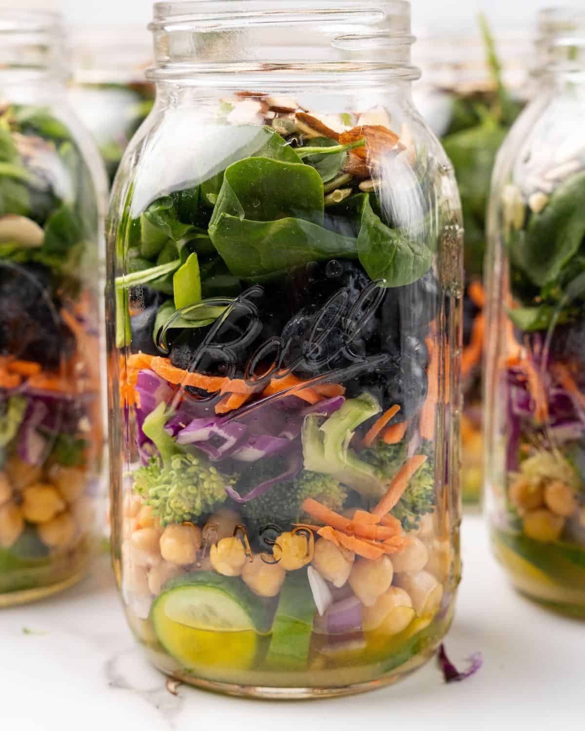 mason jar salads with the spinach and nuts on top.