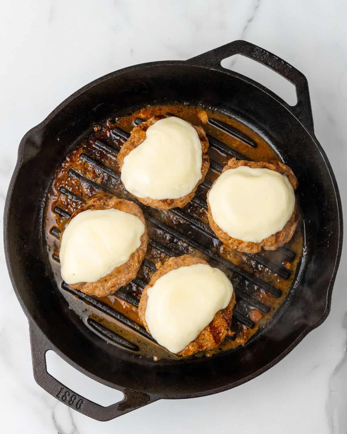 turkey burgers with melted cheese in a grill pan.