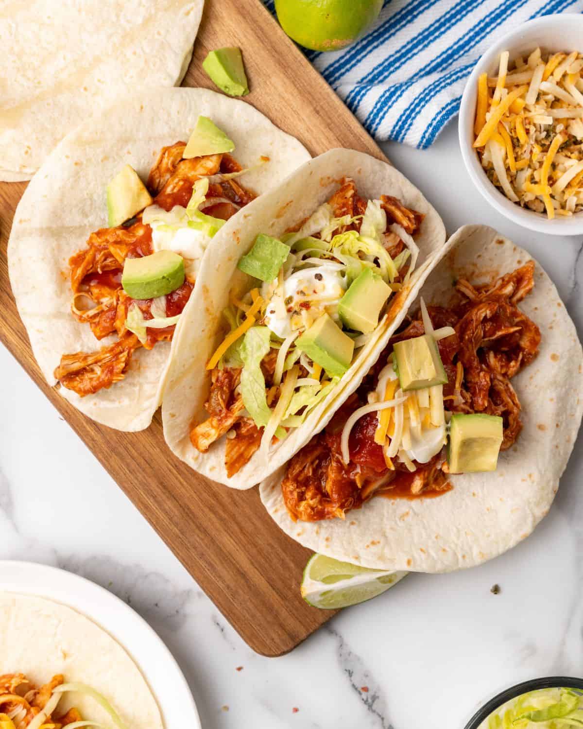 chicken tacos on a board with avocado and cheese.